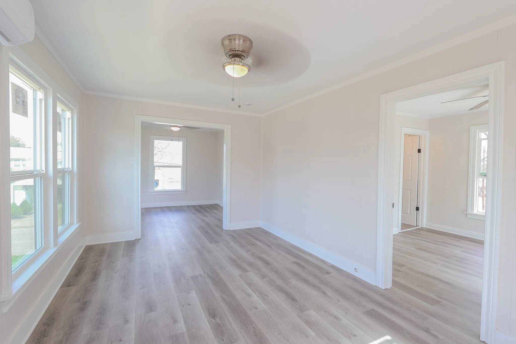 Light-toned wood-finish flooring, white window trim, and a ceiling fan with integrated lighting