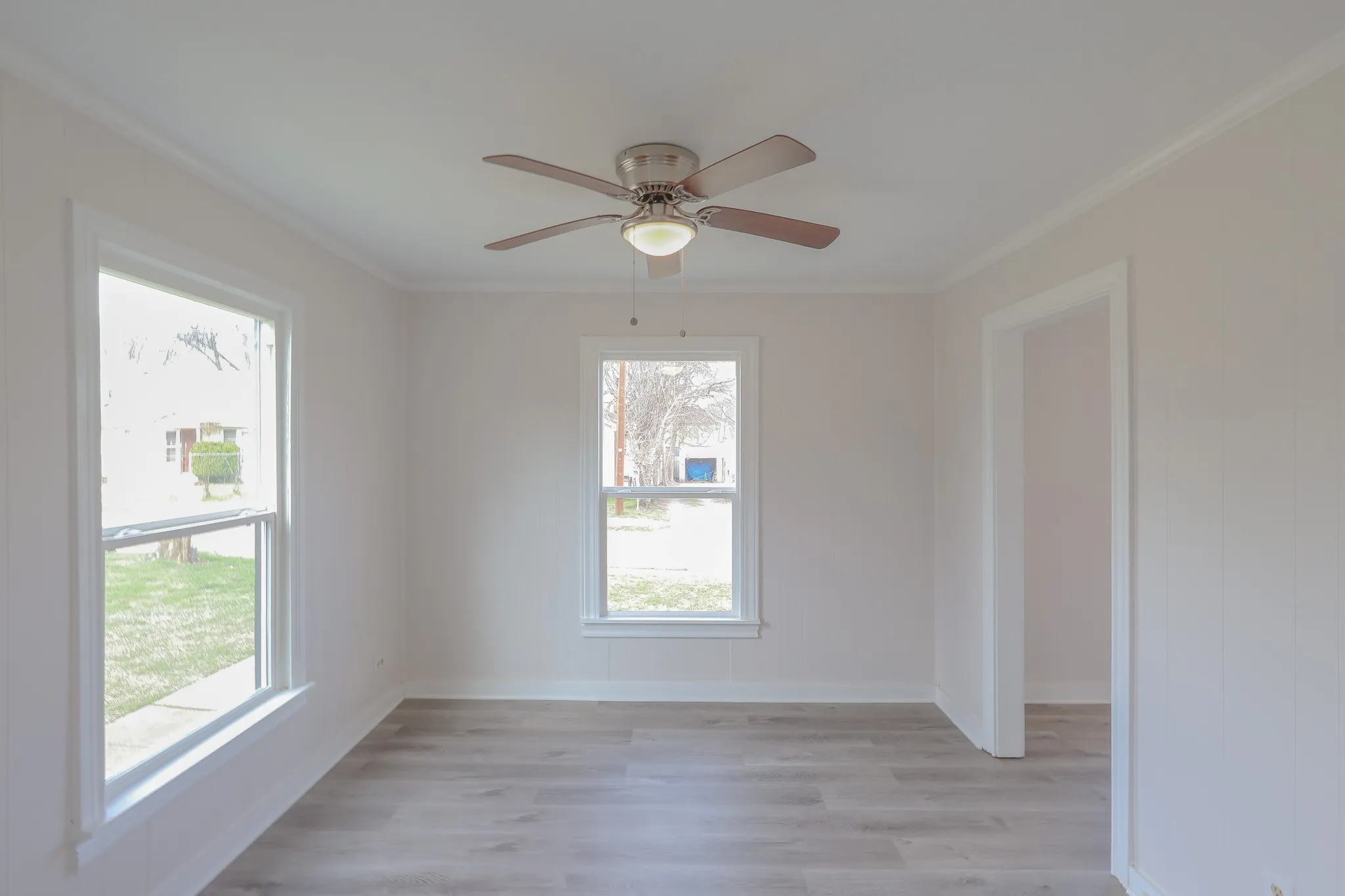 Ceiling fan with integrated lighting, wood-finish flooring, two double-hung windows, and a doorway with white trim