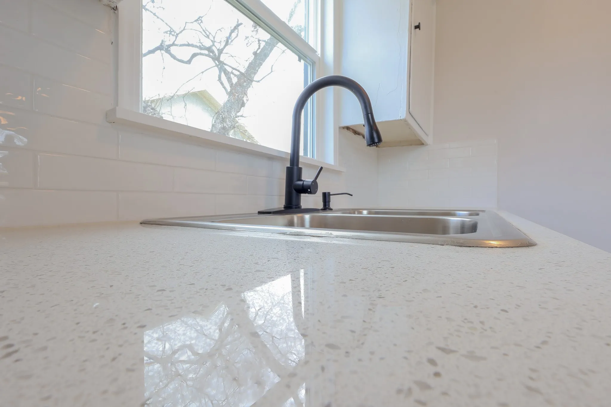 Polished stone-finish countertop, stainless steel double basin sink, matte black gooseneck faucet, and white subway tile backsplash