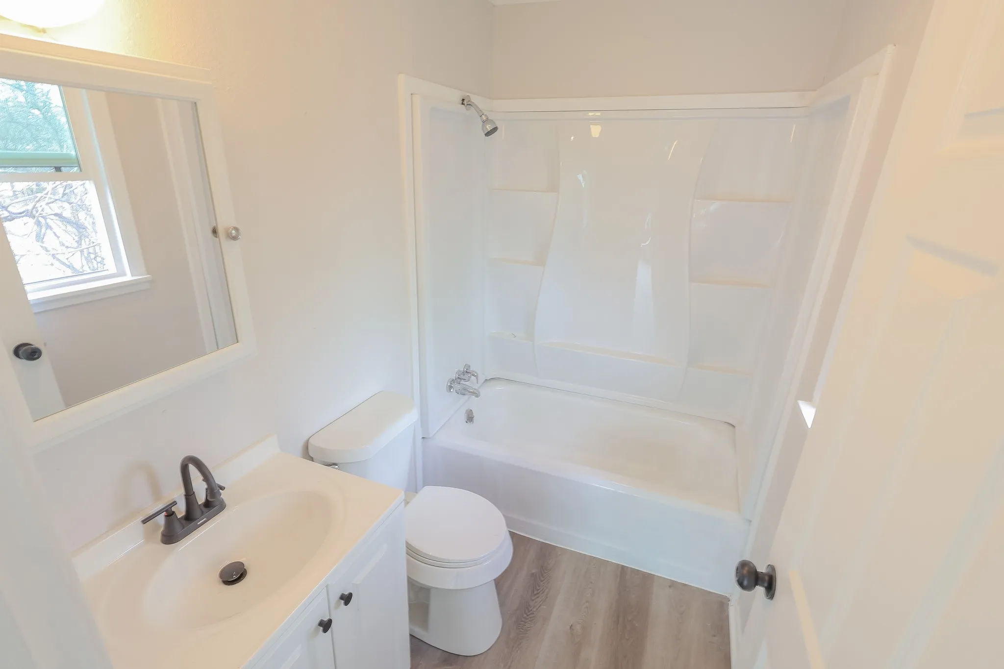 White vanity with an integrated sink and dark bronze faucet, framed mirror, and a window