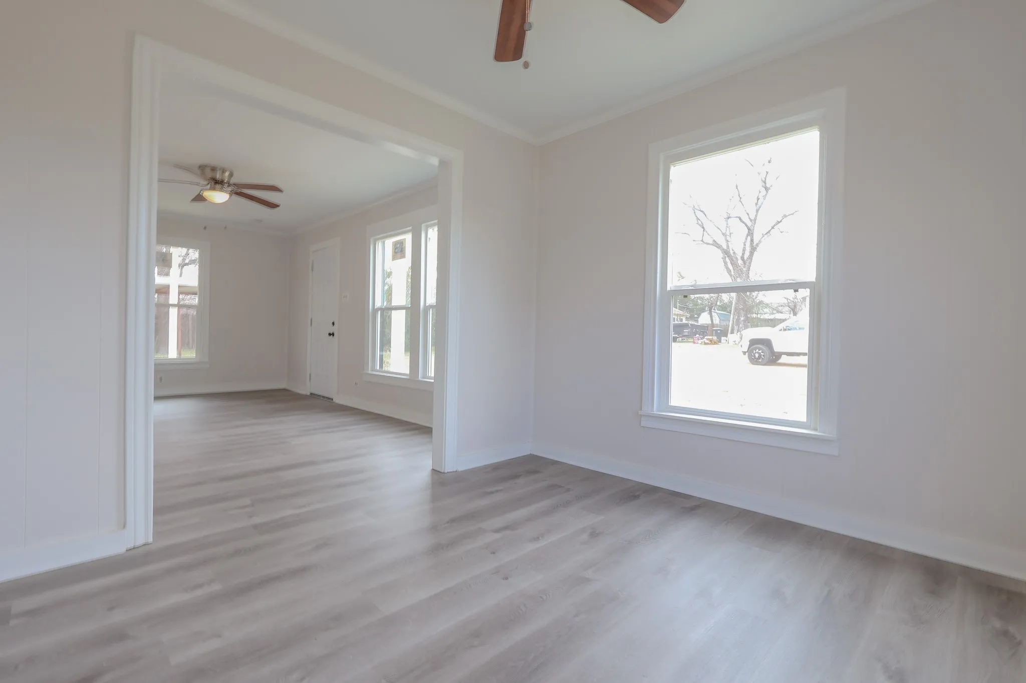 Bright, open living spaces featuring gleaming wood-finish flooring throughout, abundant natural light from multiple windows, ceiling fan, and clean white walls and trim