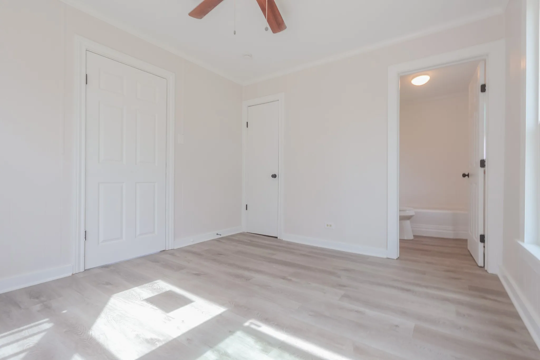 Wood-finish flooring throughout, white paneled doors, and a ceiling fan