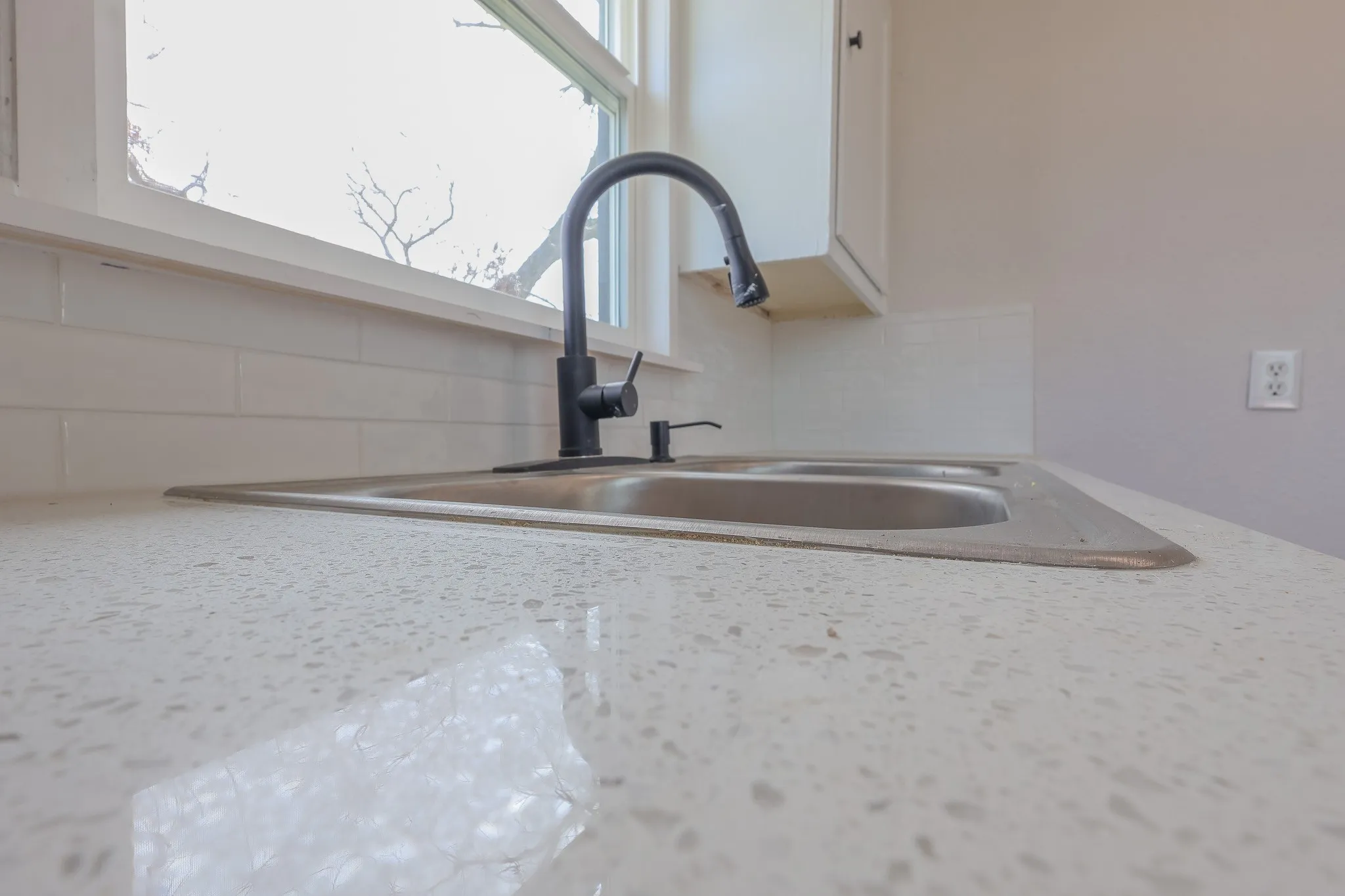 Dual-basin stainless steel sink with a matte black high-arc faucet, set within a speckled white countertop