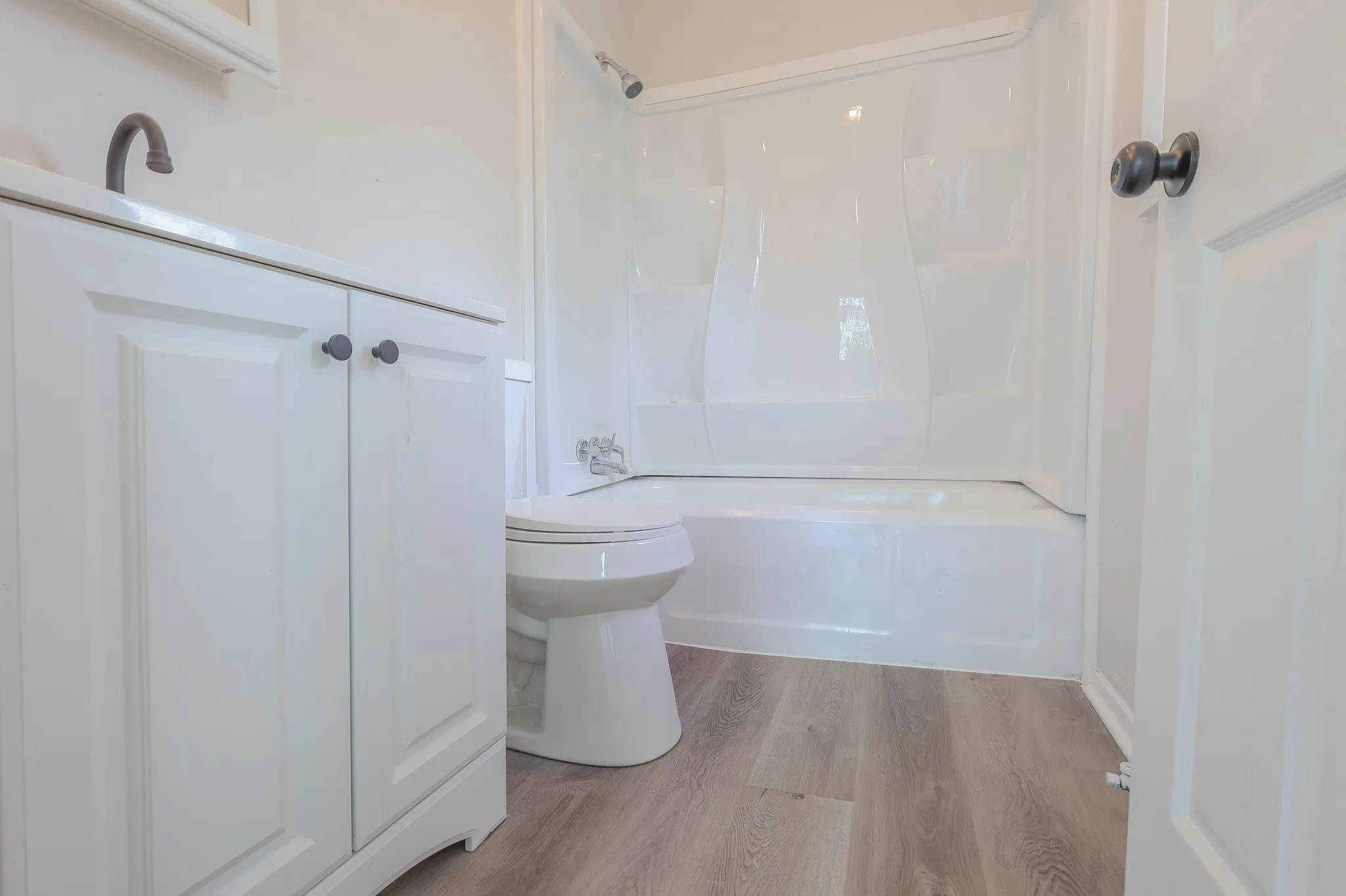 White vanity with dark hardware, white toilet, white tub-shower combination, and wood-finish flooring