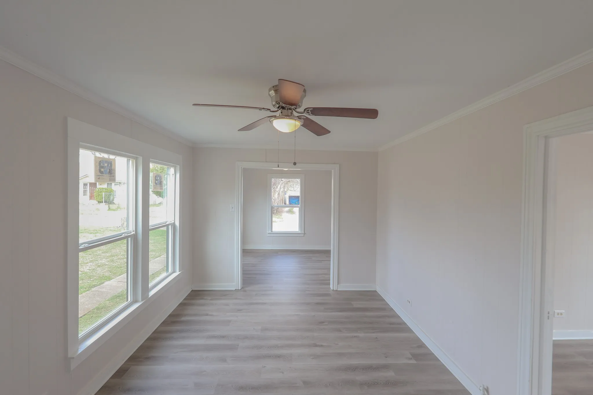 Wood-finish flooring, ceiling fan with integrated lighting, multiple windows, and white trim throughout