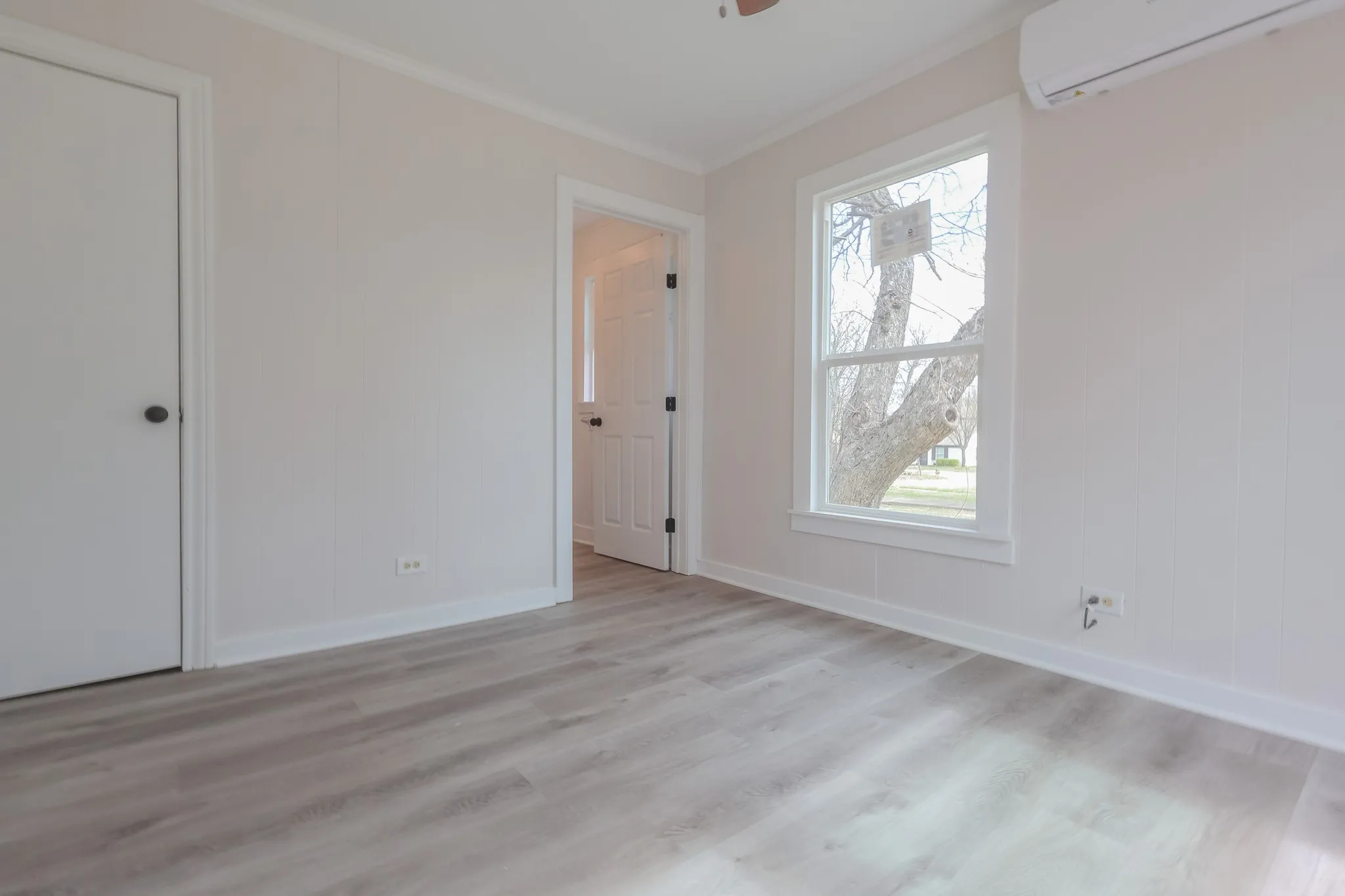 Wood-finish flooring with white trim, a double-hung window, and a wall-mounted mini-split unit