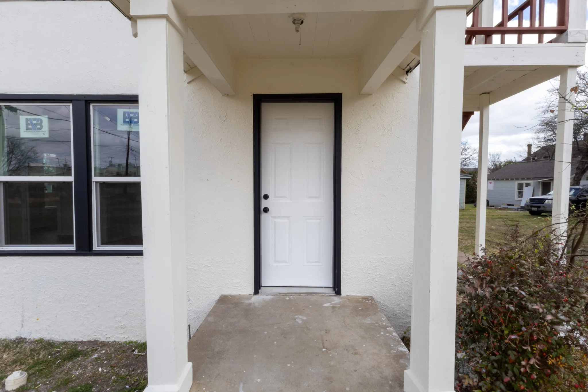 Covered entry with concrete flooring, white paneled door, and black window frames