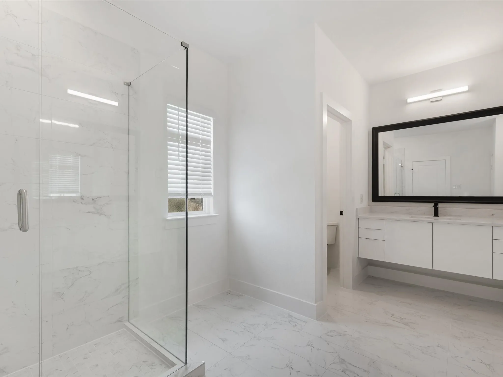 Primary Bathroom featuring light marble finish flooring, a marble finish shower, and vanity