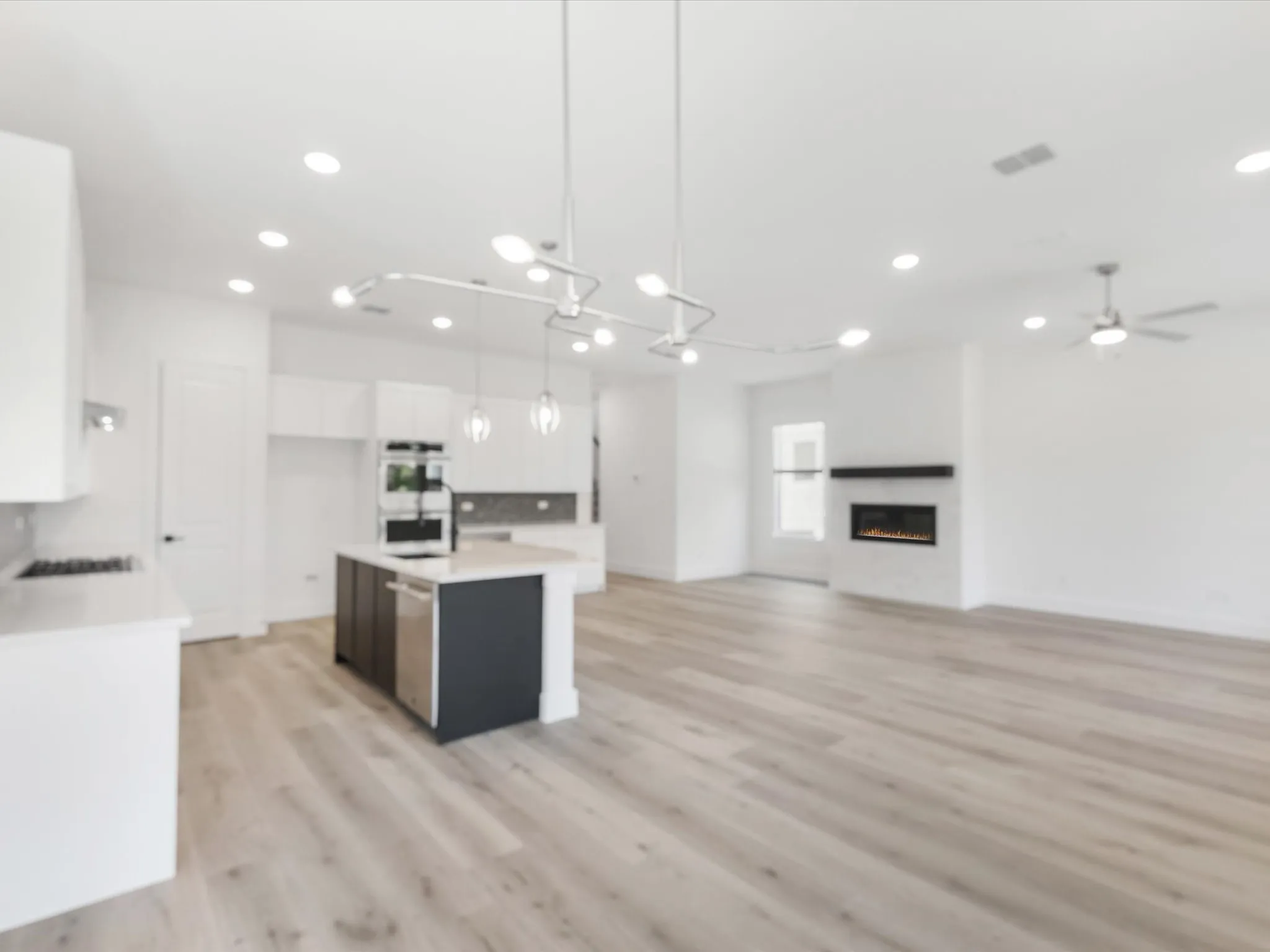 Kitchen with white cabinetry, open floor plan, a center island with sink, decorative light fixtures, and light wood-type flooring