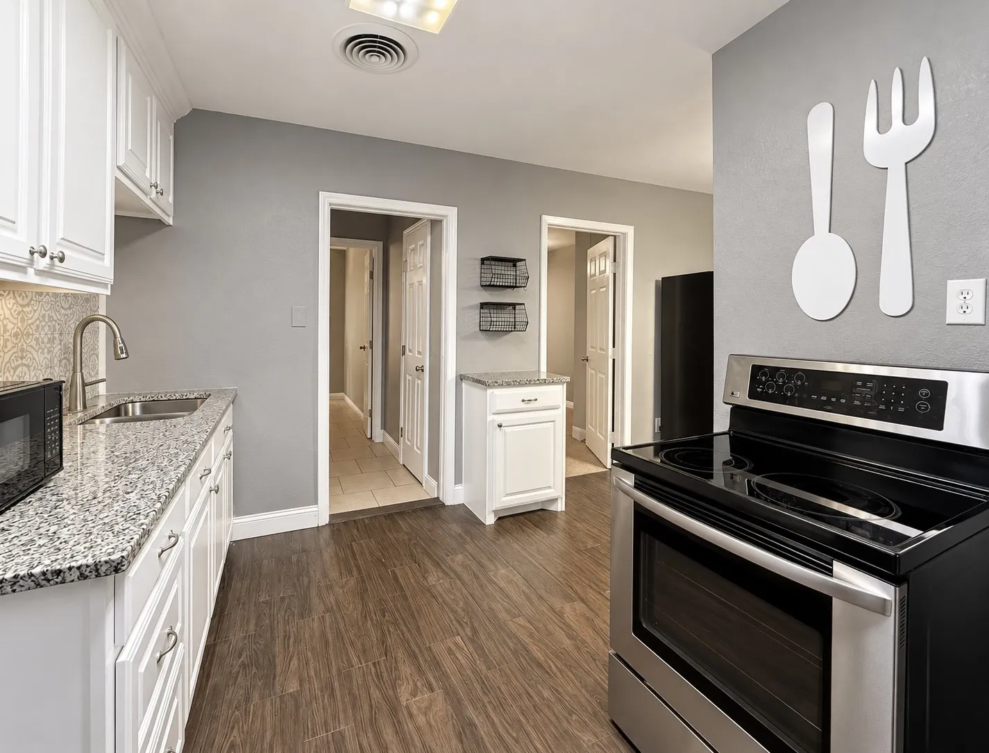 White cabinetry, stone countertops, stainless steel sink, stainless steel electric range, and wood-finish flooring