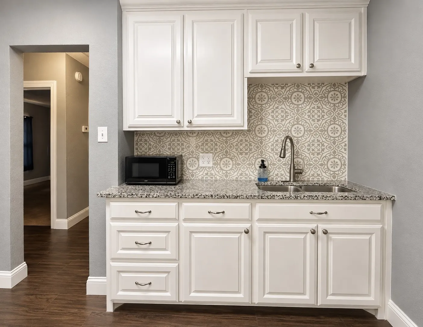 White shaker-style cabinetry, granite countertops, dual-basin stainless steel sink, decorative tile backsplash, and wood-finish flooring