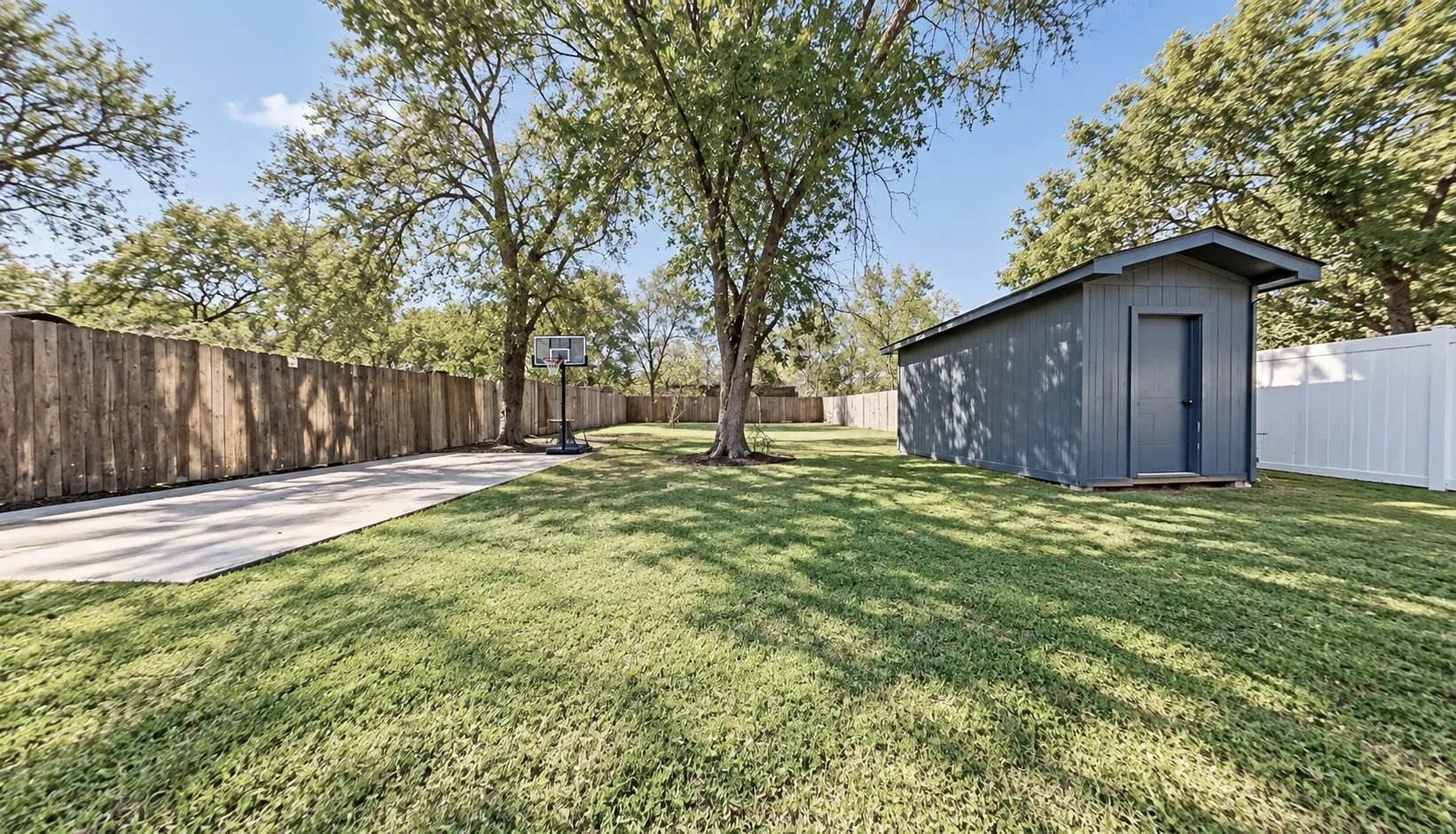 Spacious backyard featuring a large shed, concrete pad, mature trees, and privacy fencing
