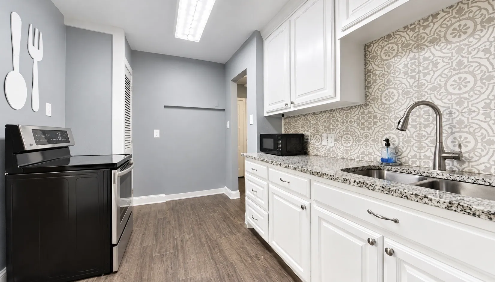 White cabinetry, patterned backsplash, stainless steel sink, granite-style countertops, and wood-finish flooring