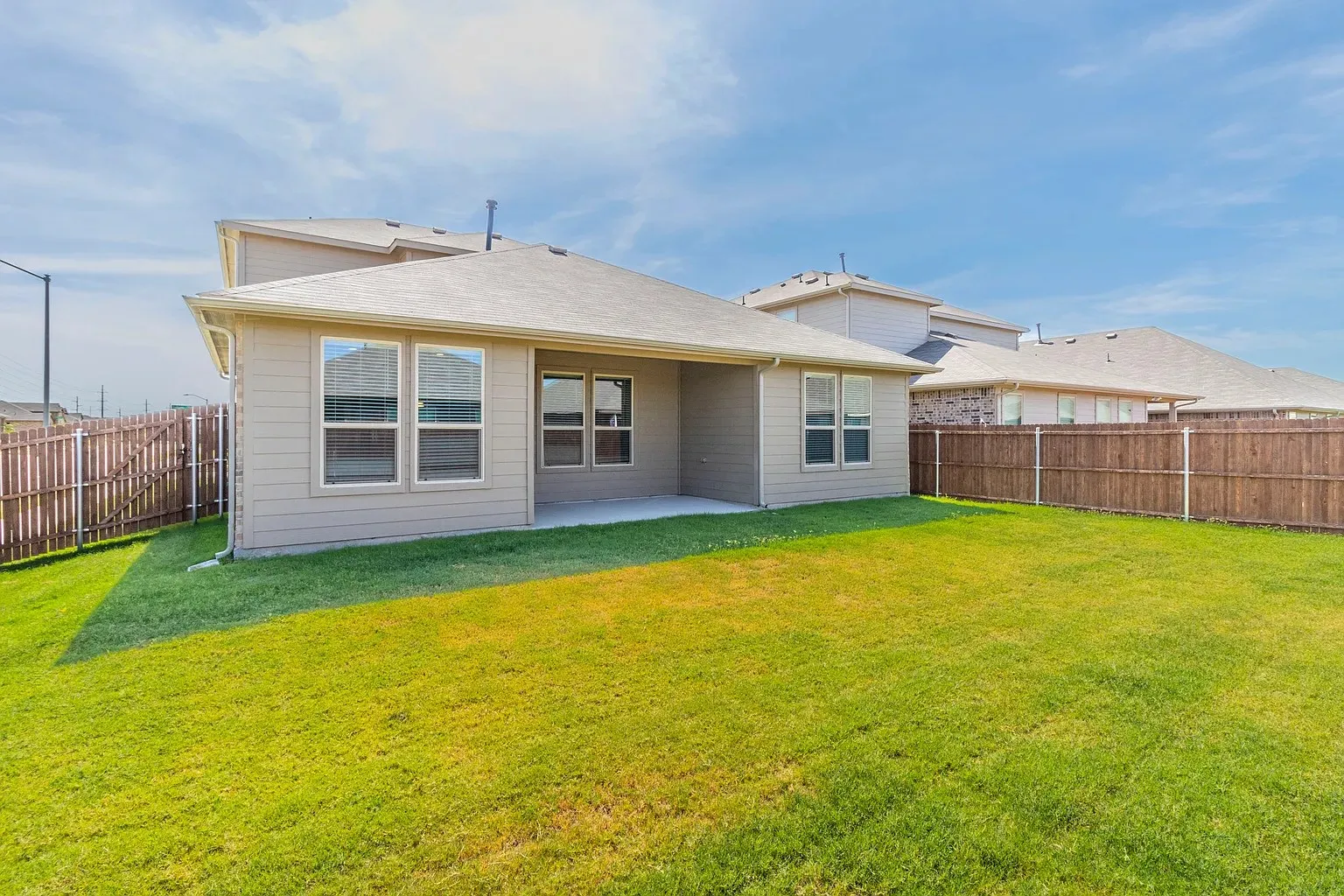 Expansive backyard featuring a covered patio, privacy fencing, and a manicured lawn