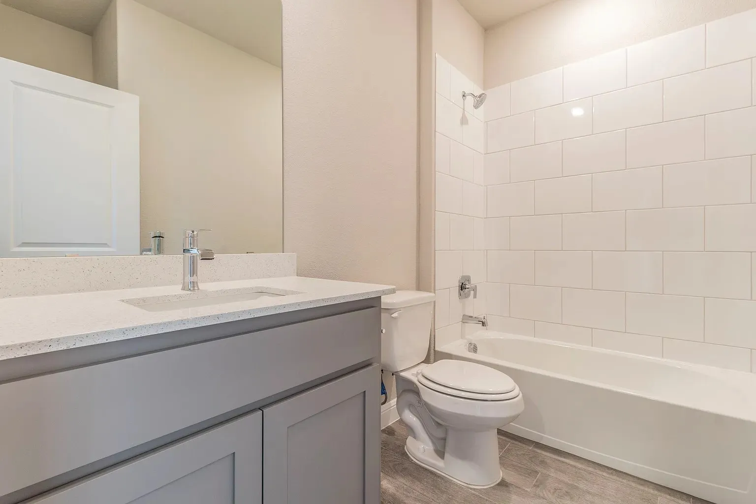 Vanity with stone-finish countertop and integrated sink, chrome faucet, full-width mirror, subway tile shower surround, and wood-finish flooring