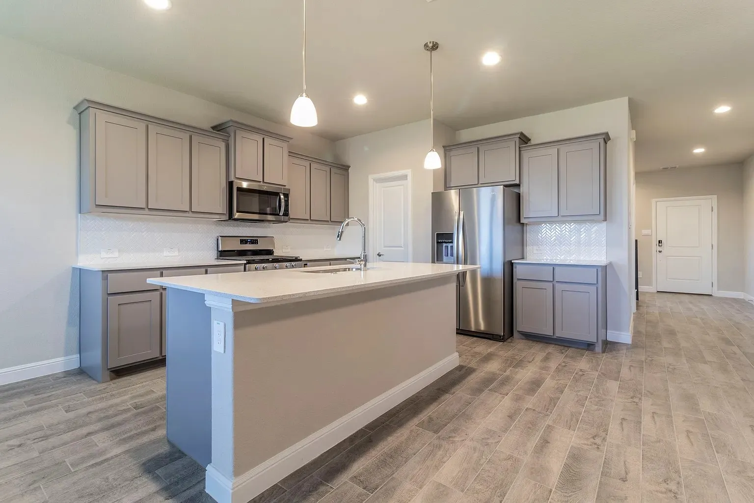 Kitchen featuring light grey cabinetry, stainless steel appliances, a white tile backsplash, and an island with a white countertop