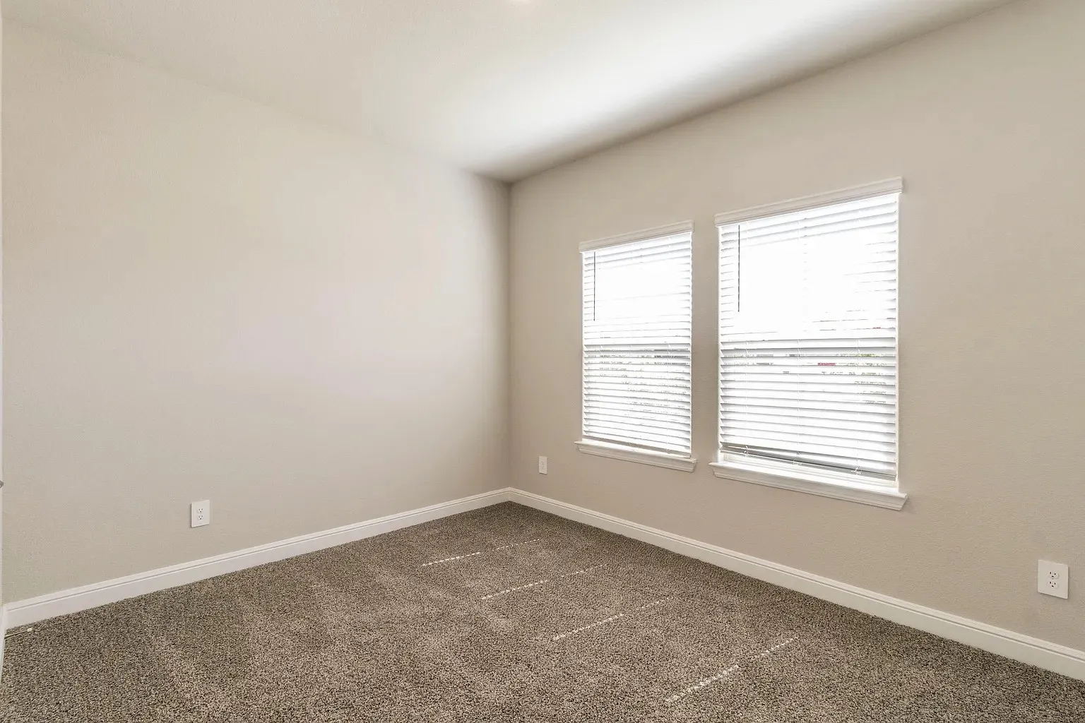 Two windows with blinds, neutral wall paint, and carpeted flooring