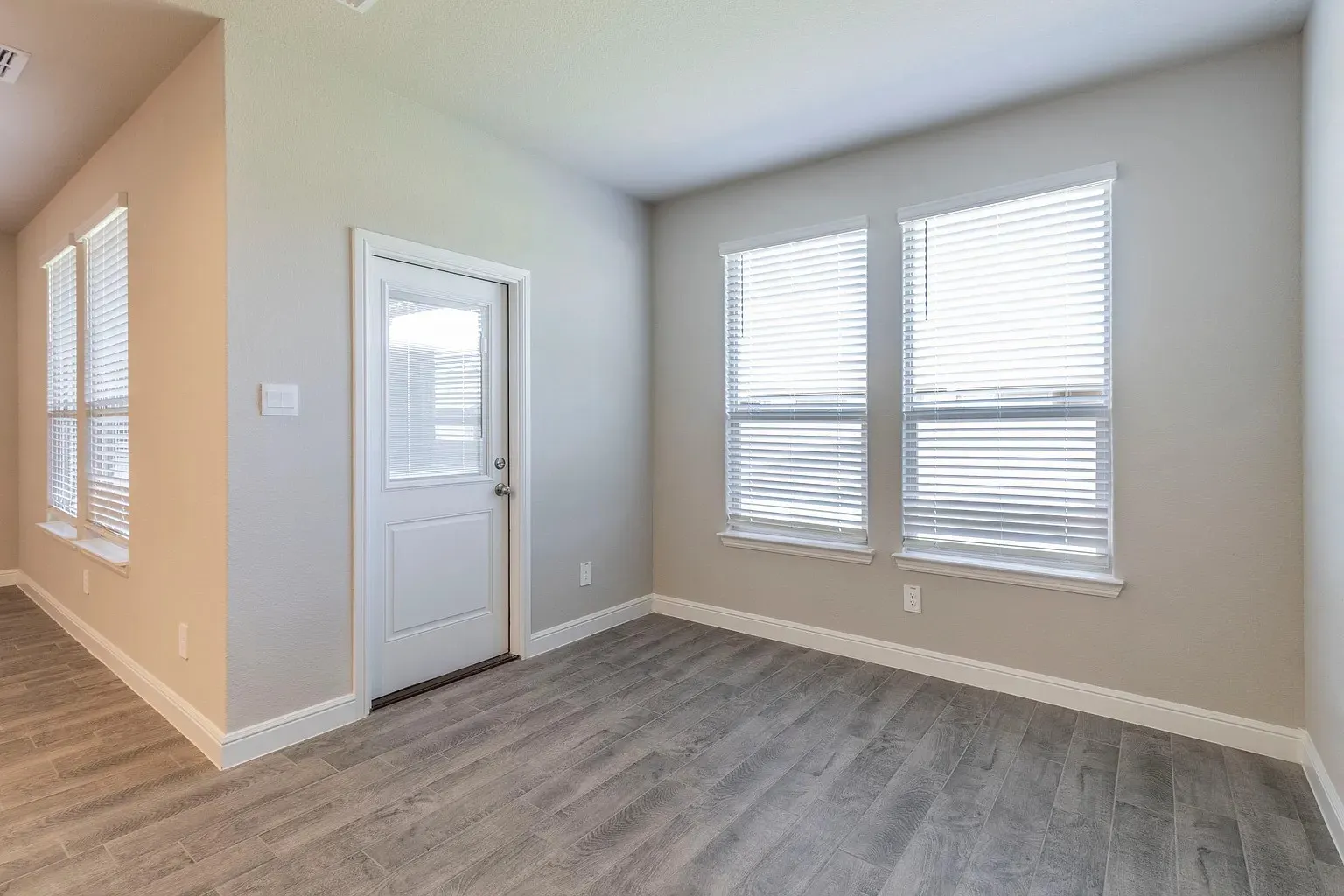 Wood-finish flooring throughout, multiple windows with blinds, and a white paneled door with a partial glass insert