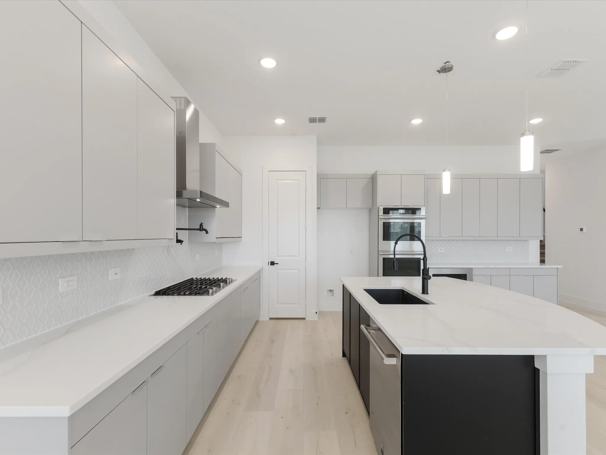 Kitchen with tasteful backsplash, modern cabinets, hanging light fixtures, light wood-style flooring, and light stone countertops