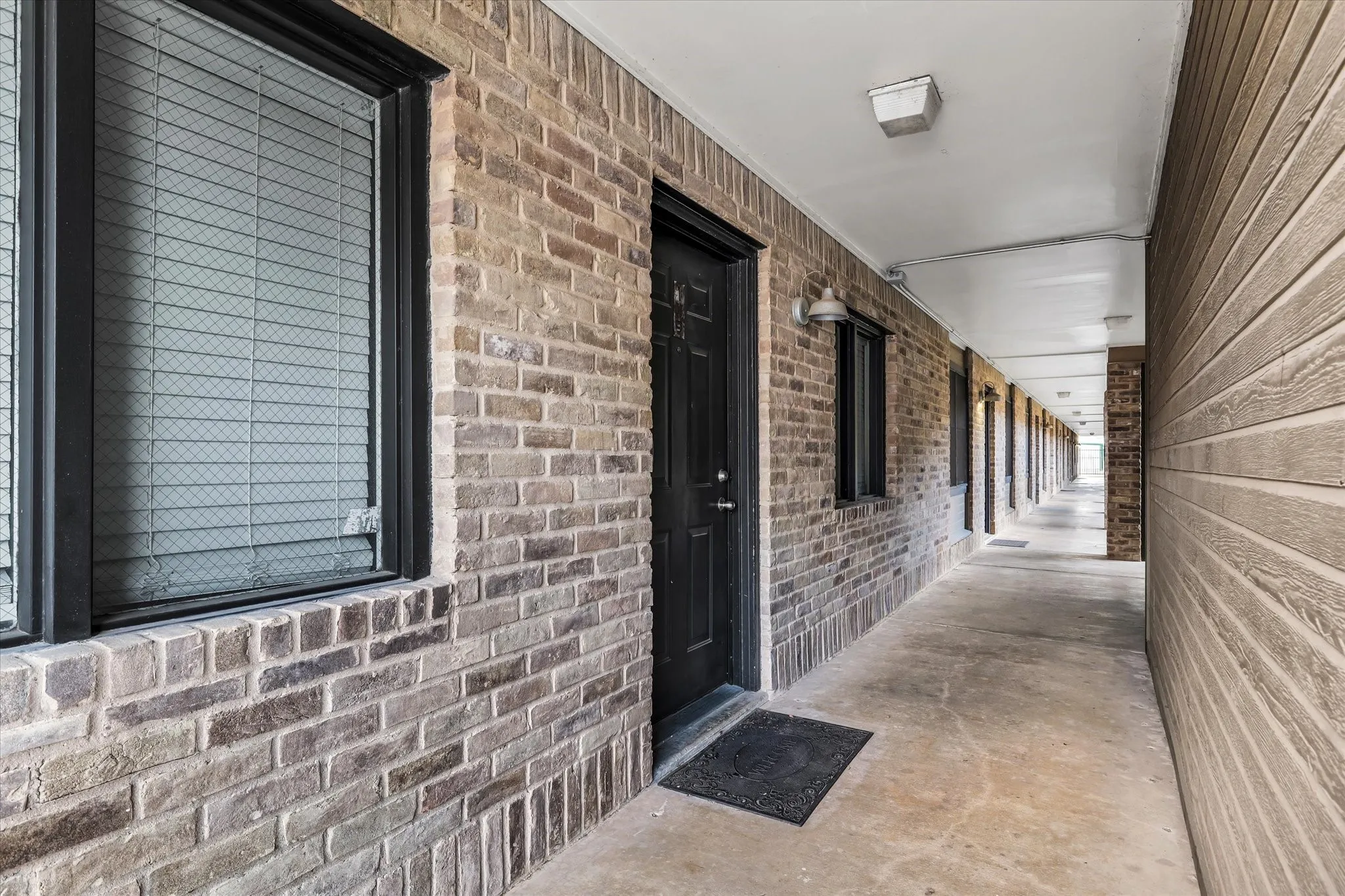 Brick exterior facade with black window frames, sconce lighting, and a concrete walkway