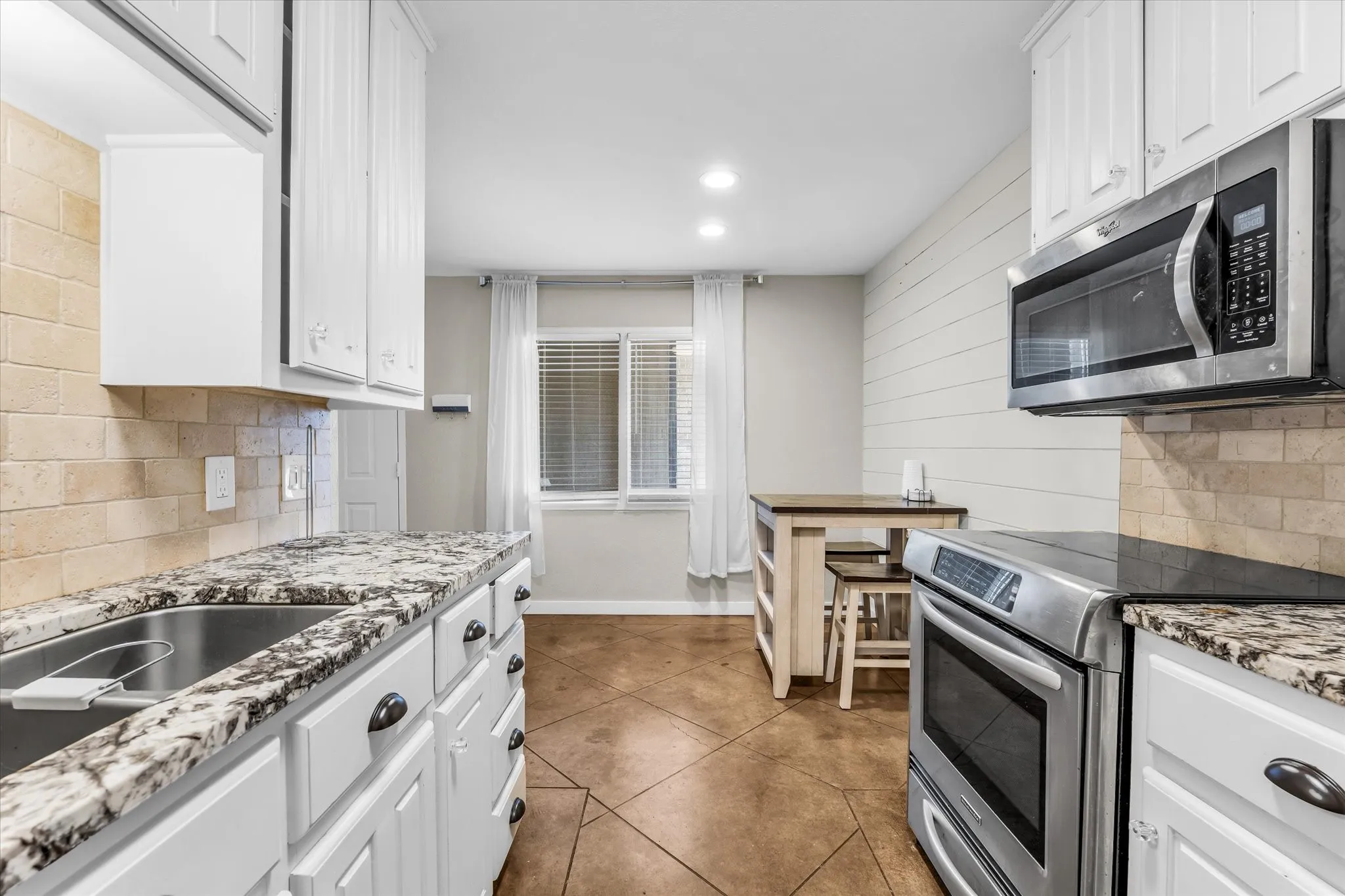 White cabinetry, granite-finish countertops, stainless steel appliances, brick-patterned tile backsplash, and wood-finish flooring
