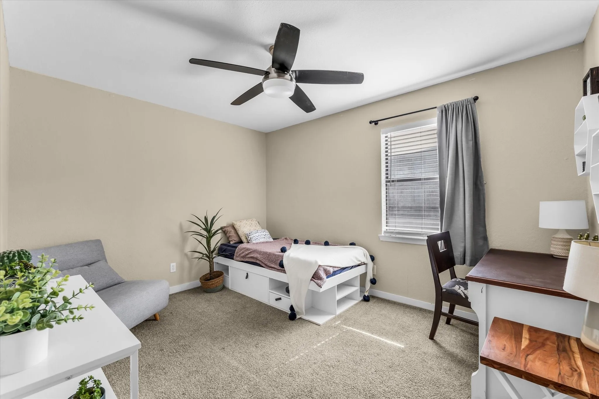 Neutral tone wall paint, carpet flooring, window with blinds, ceiling fan, and built-in storage beneath the bed frame