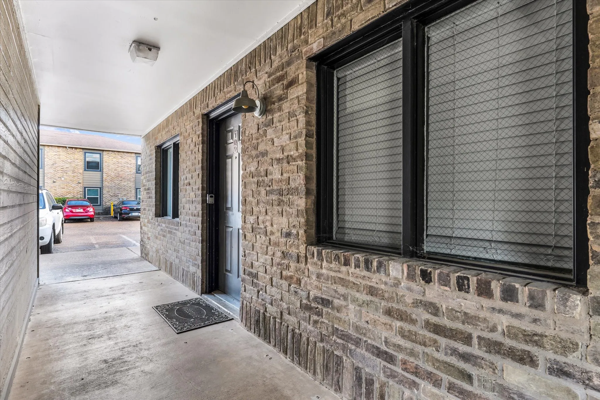 Brick exterior with black window frames, an overhead light fixture, and a surface-mounted exterior light