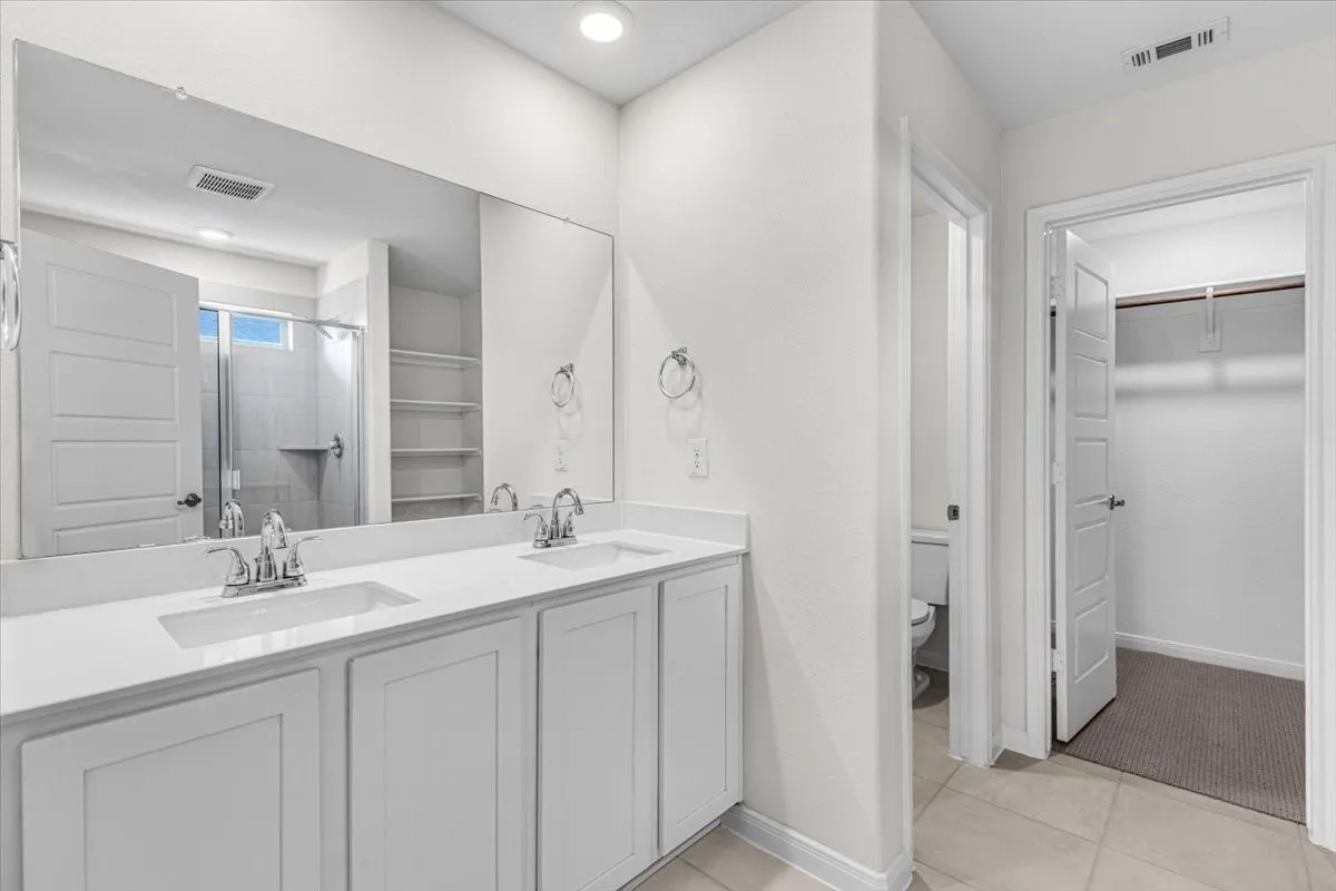 Elegant master bathroom with dual sinks, large shower, and private toilet area