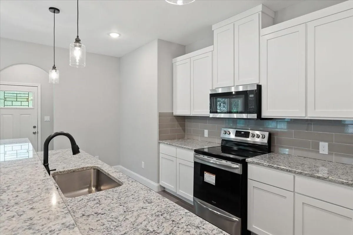 Kitchen featuring white shaker cabinetry, stainless steel appliances, granite countertops, a subway tile backsplash, and pendant lighting