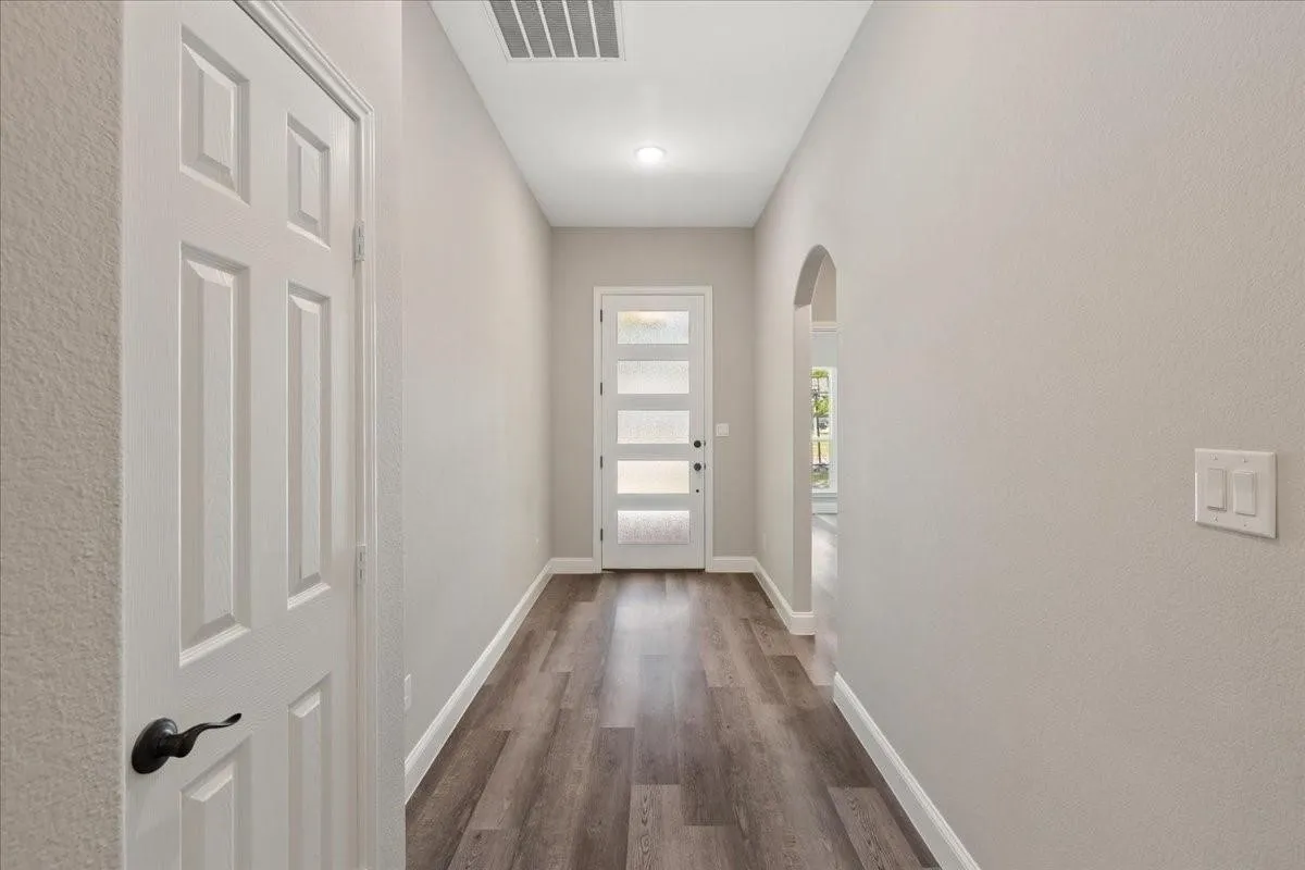 Entryway featuring wood-finish flooring, a modern front door with frosted glass panels, and an arched doorway