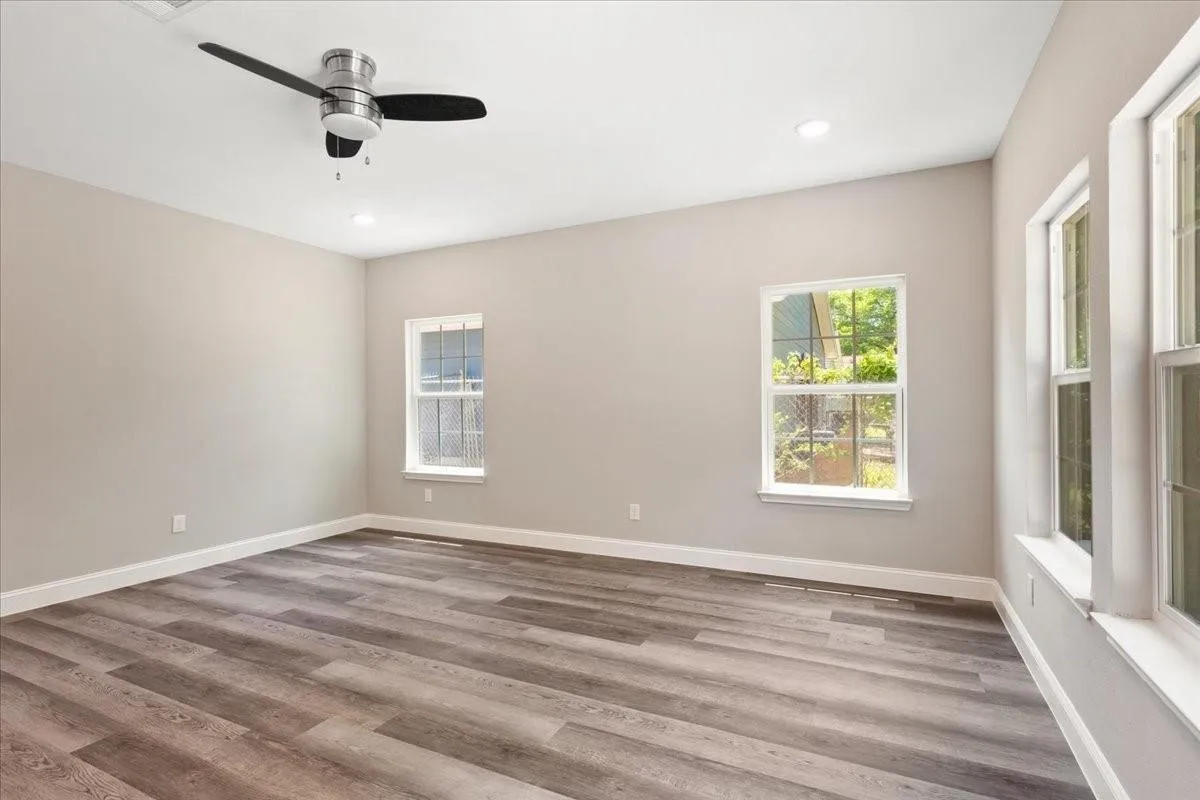 Spacious room featuring wood-finish flooring, light neutral wall paint, a ceiling fan, recessed lighting, and multiple windows