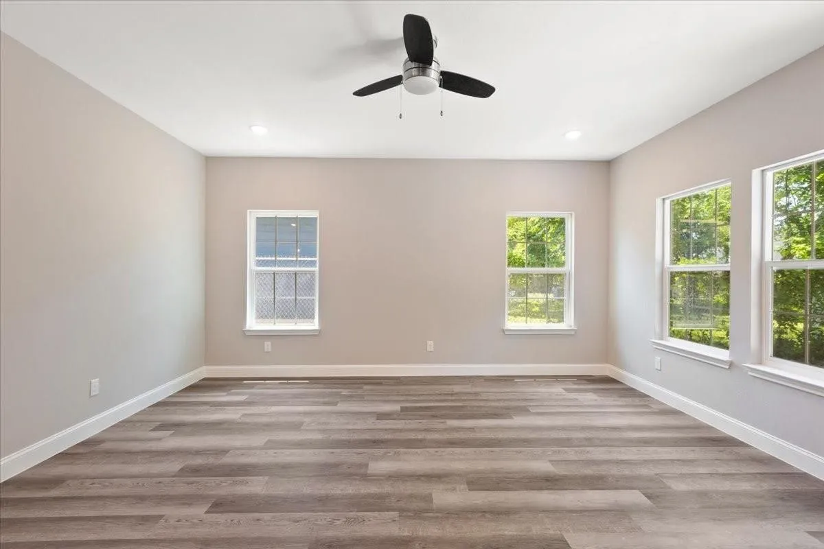 Spacious room featuring wood-finish flooring, multiple windows, a ceiling fan, and recessed lighting