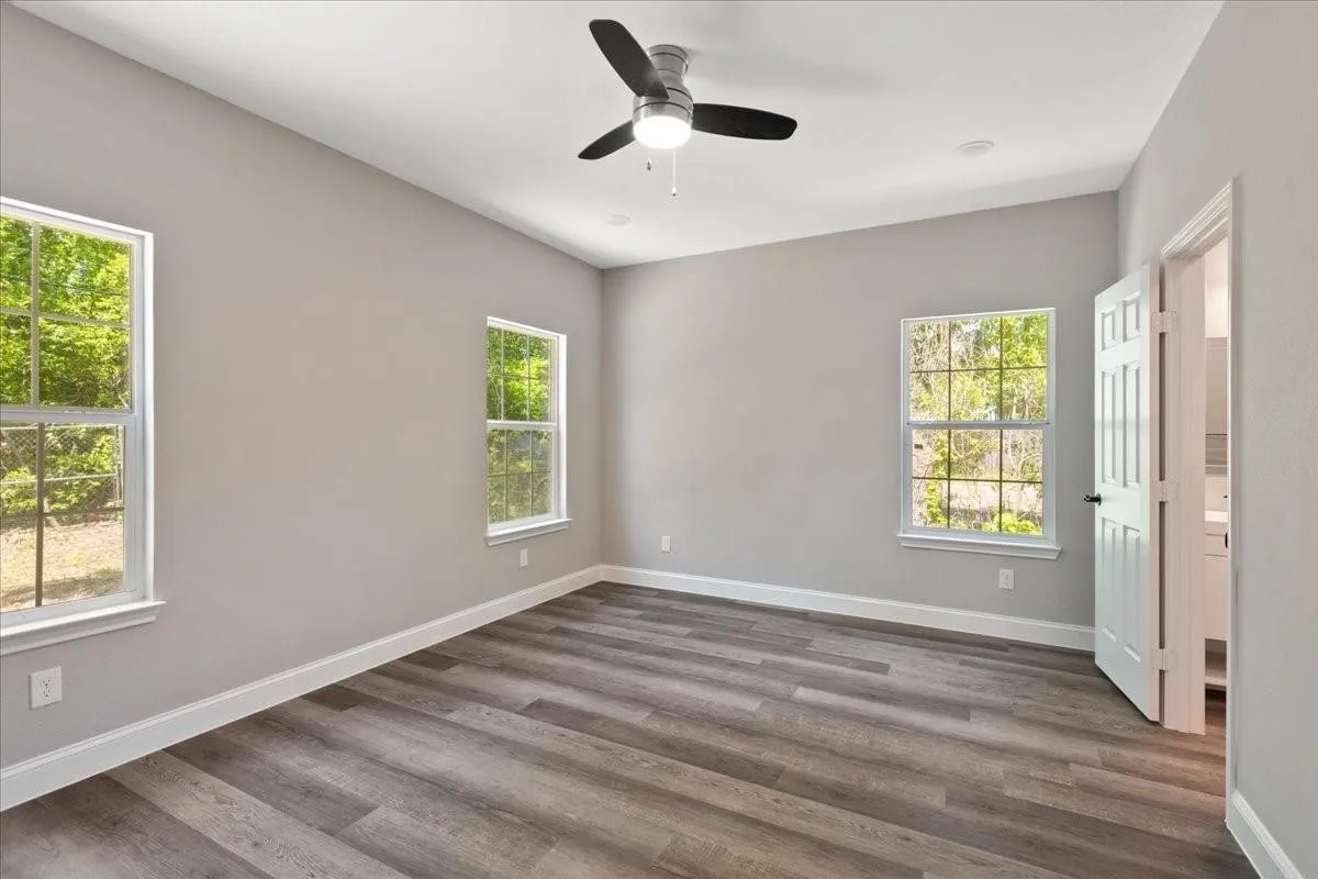 Spacious room featuring wood-finish flooring, two windows with white trim, and a ceiling fan with integrated lighting