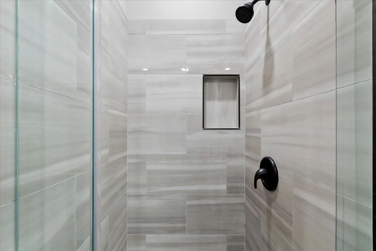 Glass-enclosed shower with horizontally-laid tile, recessed lighting, a built-in niche, and matte black fixtures