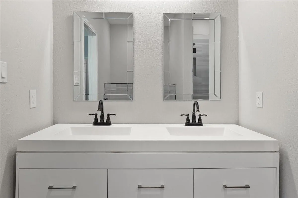 Dual white integrated sinks with dark bronze fixtures set in a white vanity with paneled drawer fronts and dark bronze pulls