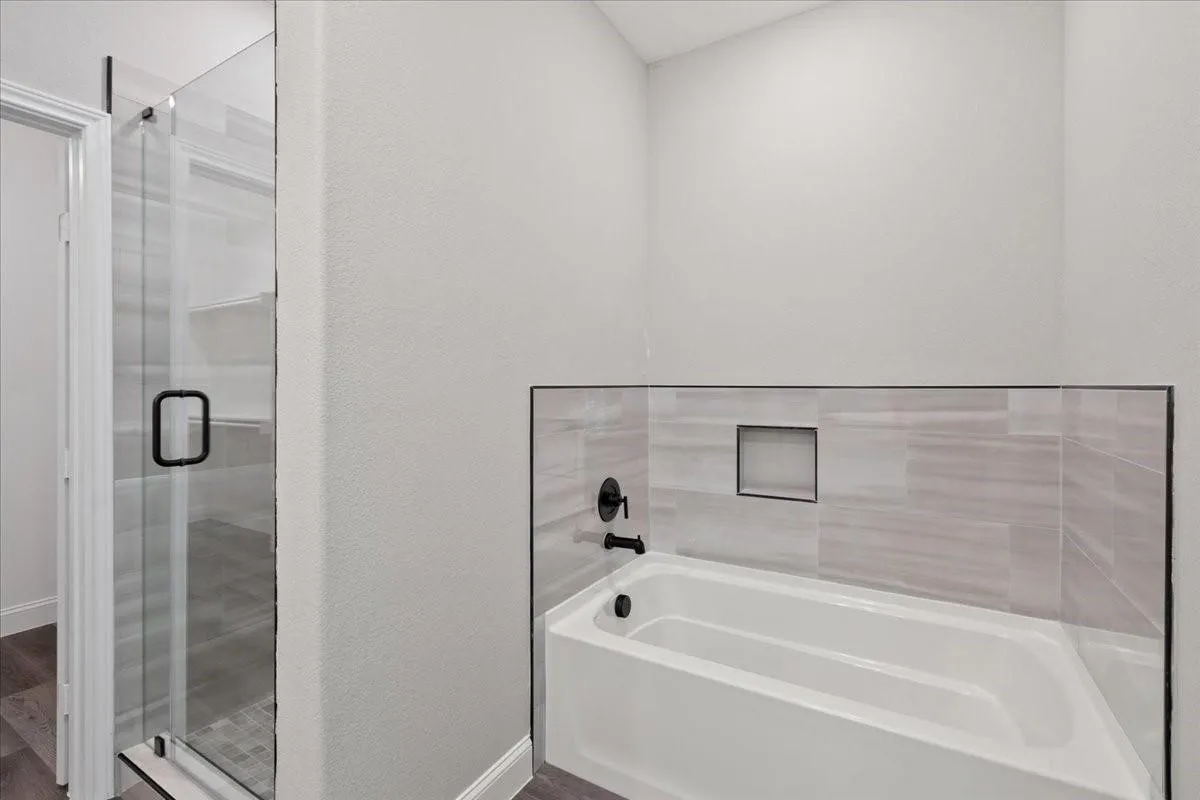 Glass-enclosed shower with matte black hardware, tiled shower floor, built-in bathtub with matte black fixtures, and tiled surround with integrated niche