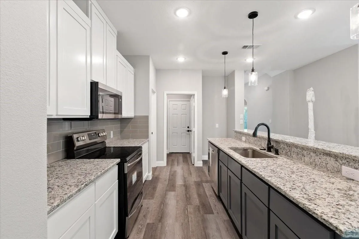 Kitchen featuring granite countertops, wood-finish flooring, stainless steel appliances, white upper cabinetry, and dark lower cabinetry