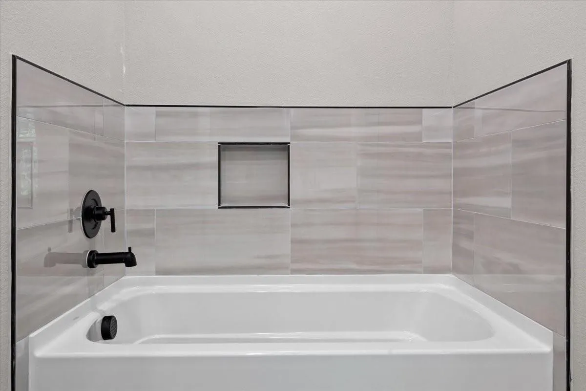 Bathtub with light-toned rectangular wall tiling, matte black fixtures, and a recessed shower niche