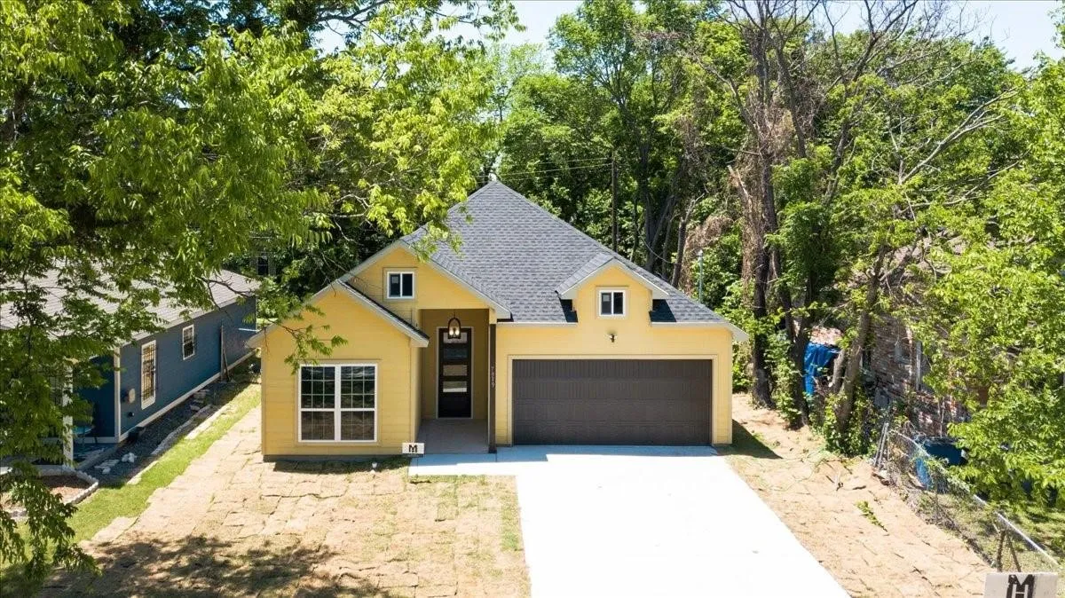 Single-story residence featuring a gray shingle roof, yellow exterior siding, a two-car garage, and a concrete driveway