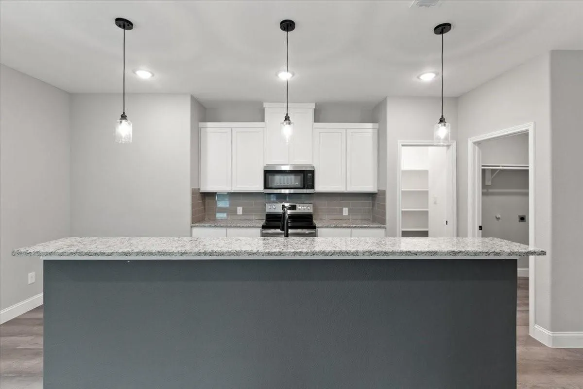 Kitchen featuring a gray island with a light-toned countertop, white cabinetry, a tile backsplash, and stainless steel appliances
