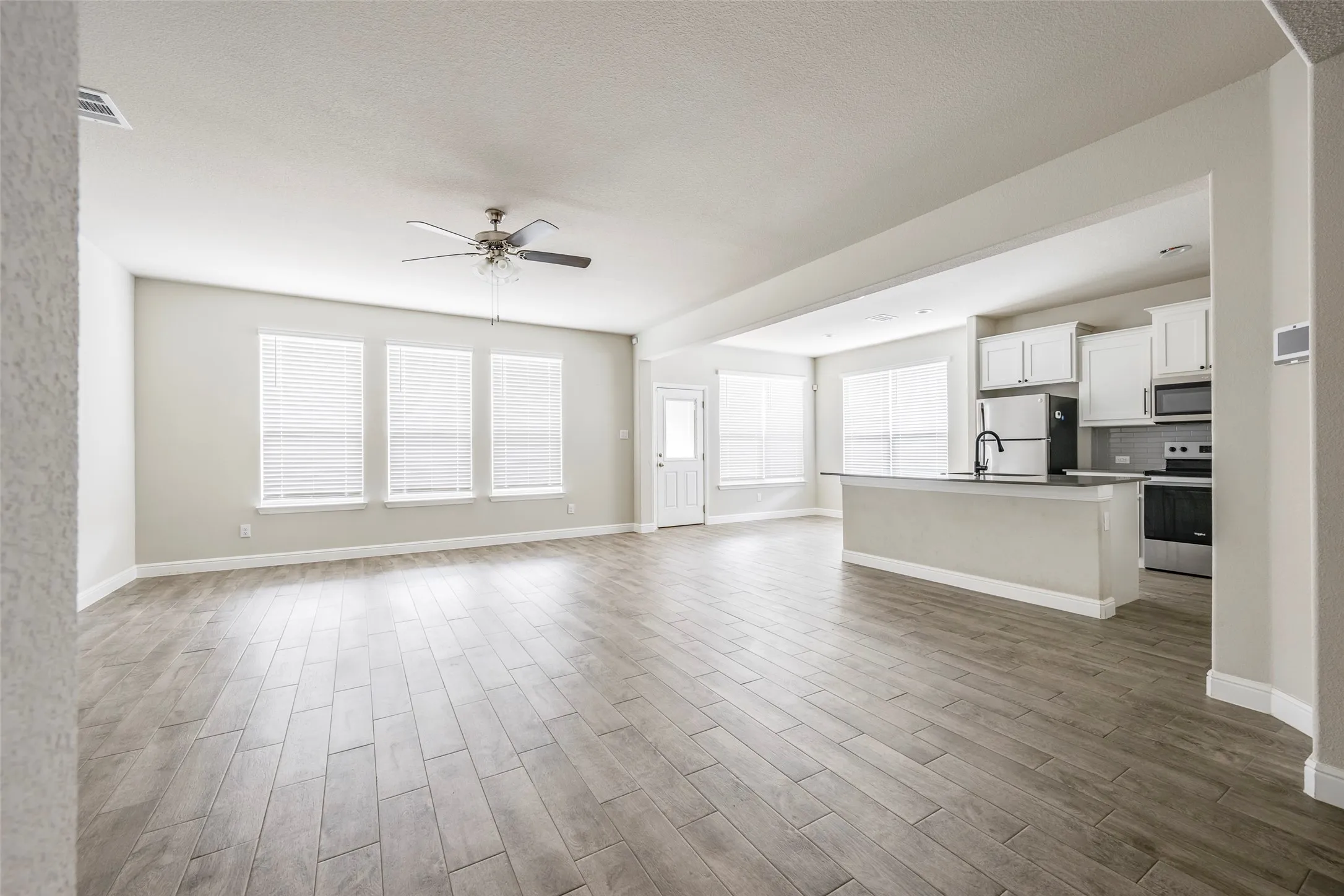Open concept living space featuring wood-finish flooring, a ceiling fan, and multiple windows with blinds