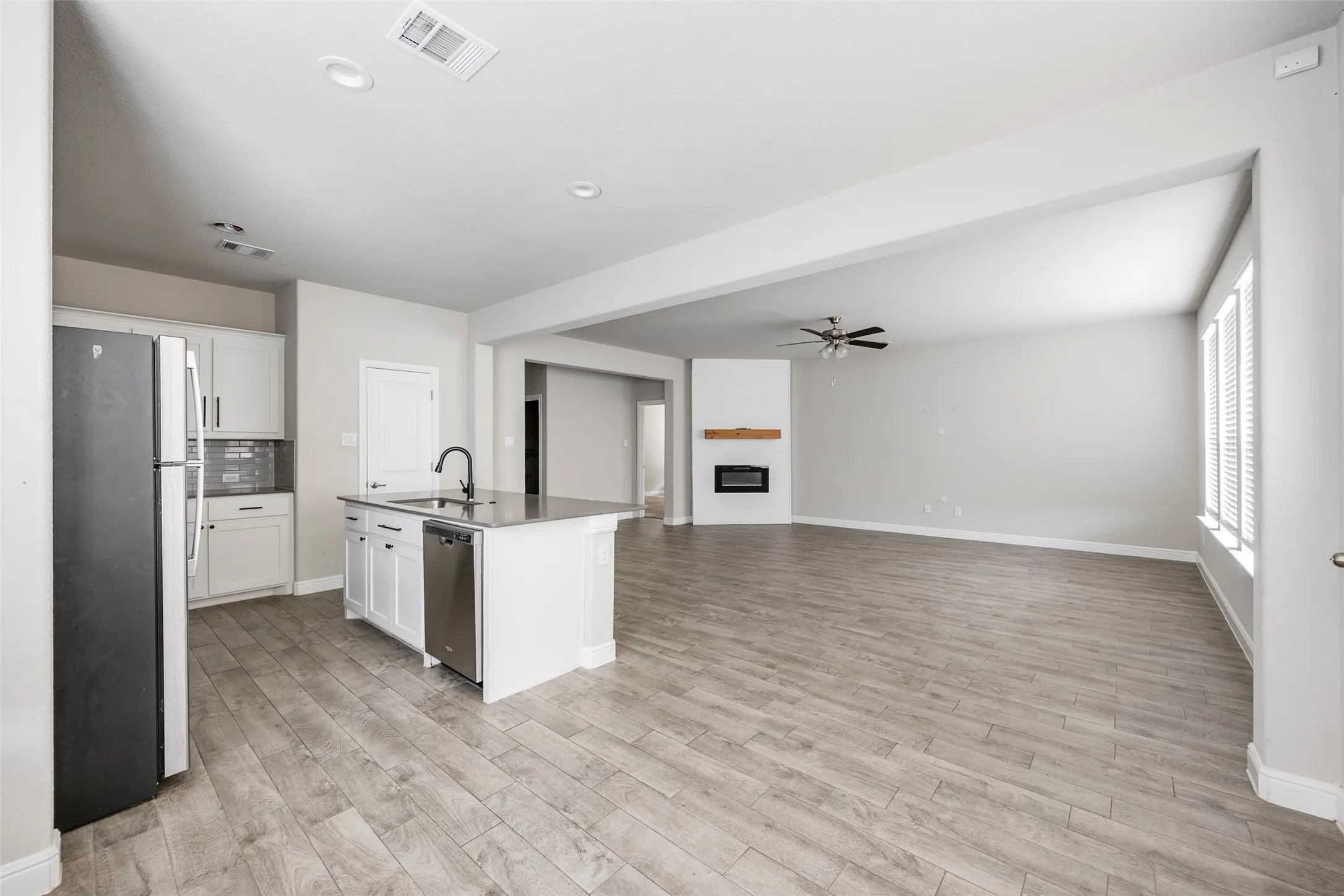 Open-concept living space featuring wood-finish flooring, a kitchen island with sink and integrated dishwasher, recessed lighting, and a fireplace with a wood mantle