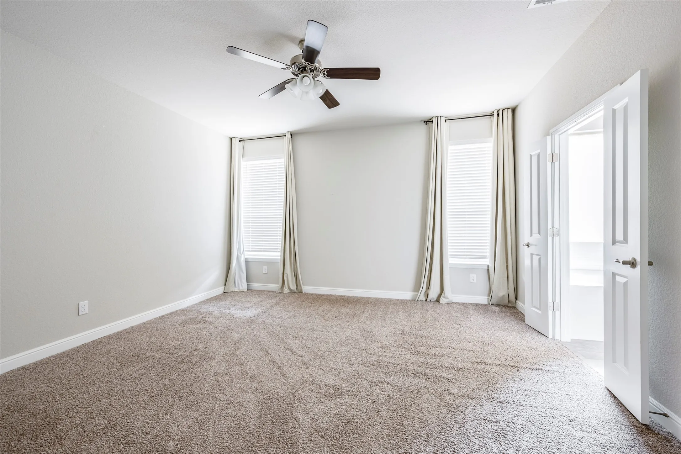 Spacious room featuring neutral carpeting, light-toned walls, and a ceiling fan with integrated lighting
