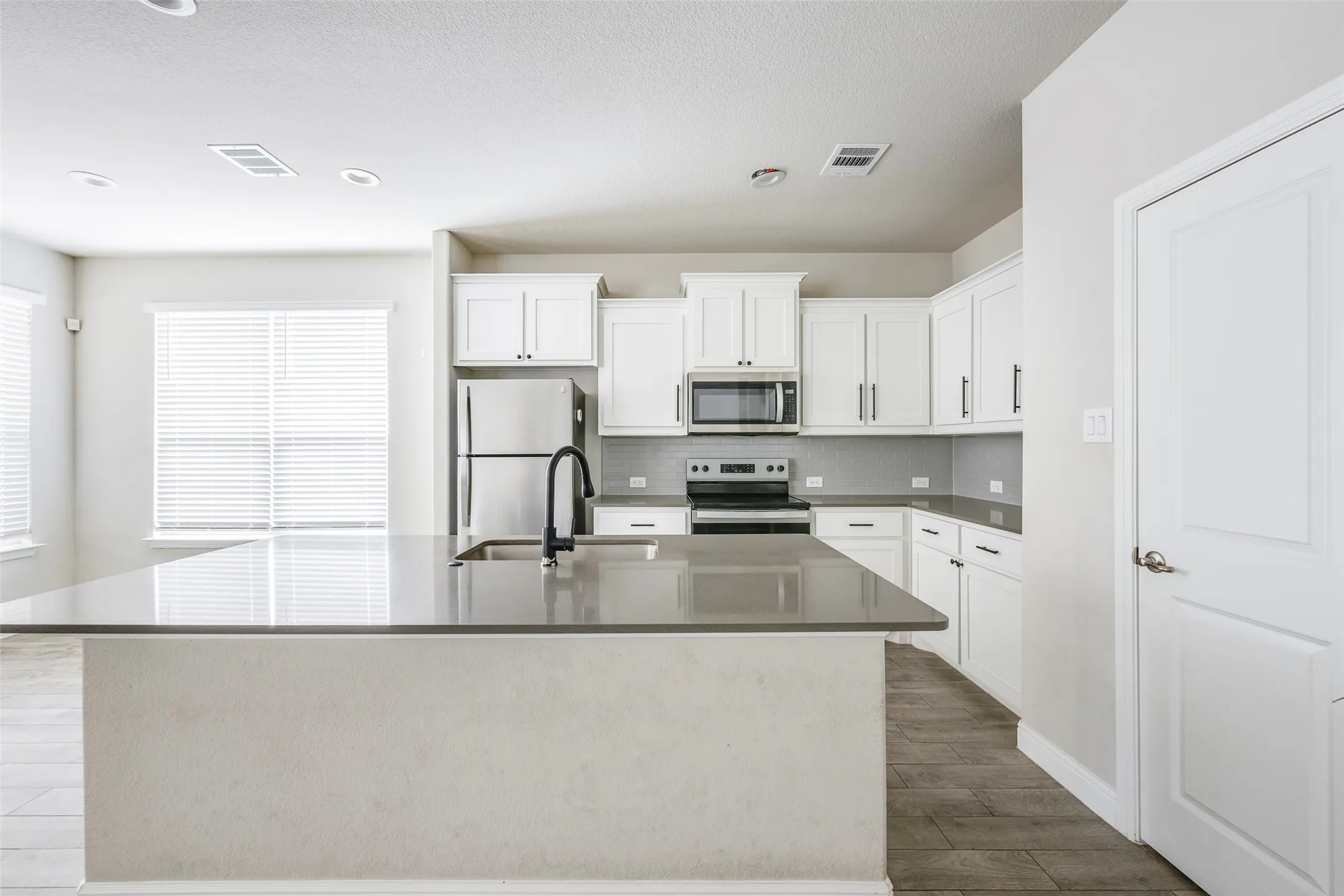 Kitchen featuring a large island with a sink, stainless steel appliances, white cabinetry, and wood-finish flooring