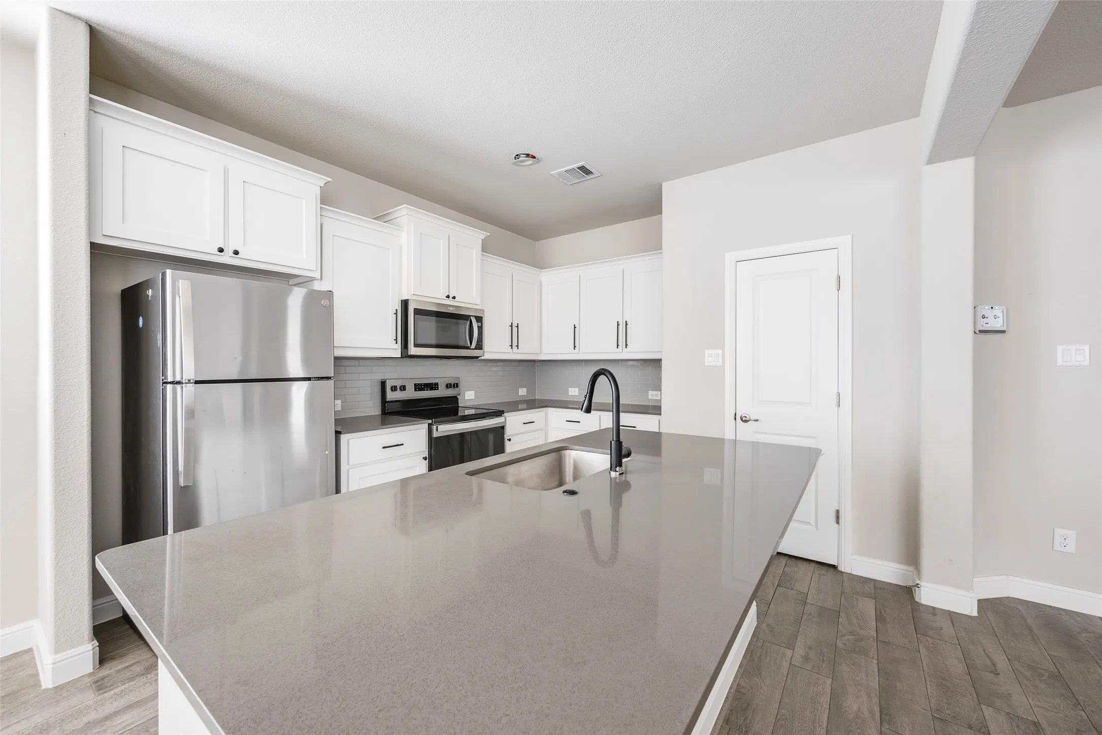 Kitchen featuring white cabinetry, stainless steel appliances, a grey tile backsplash, grey countertops, and wood-finish flooring