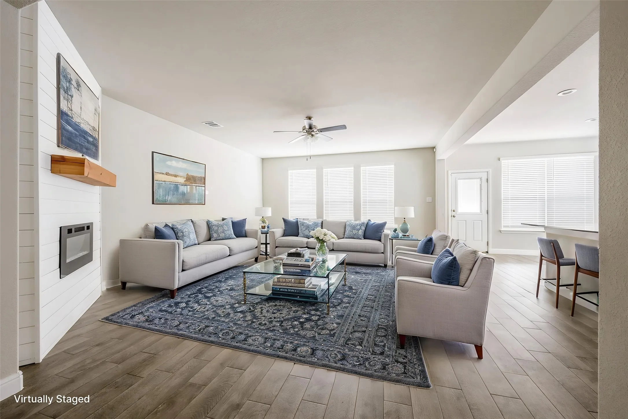 Open-concept living space featuring wood-finish flooring, a contemporary fireplace with a shiplap surround, and a ceiling fan