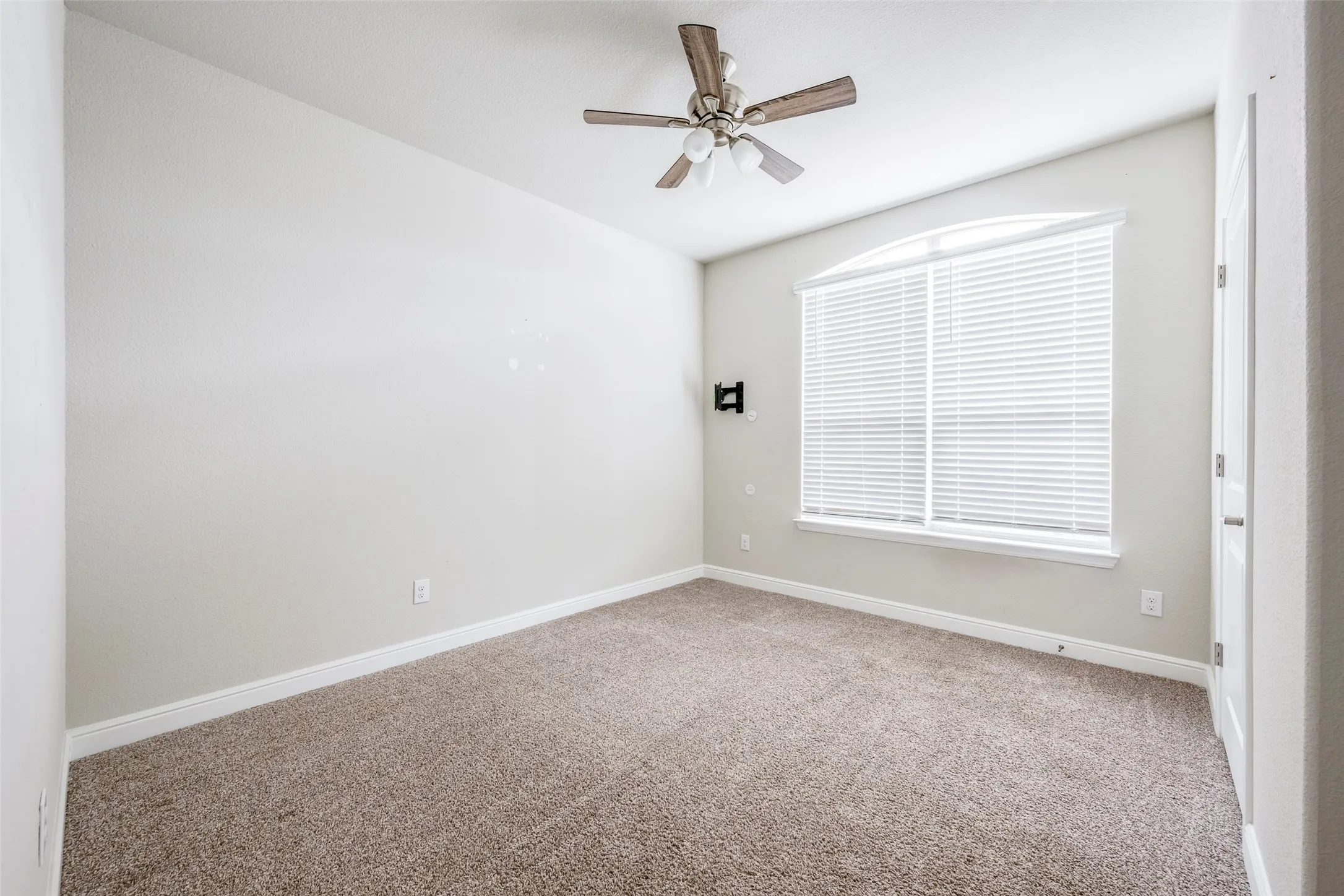 Arched window with blinds, ceiling fan with light fixture, and carpeted flooring