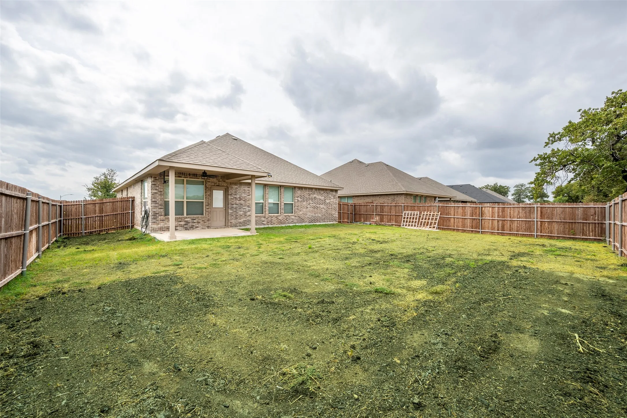 Expansive fenced backyard with a covered patio and brick exterior