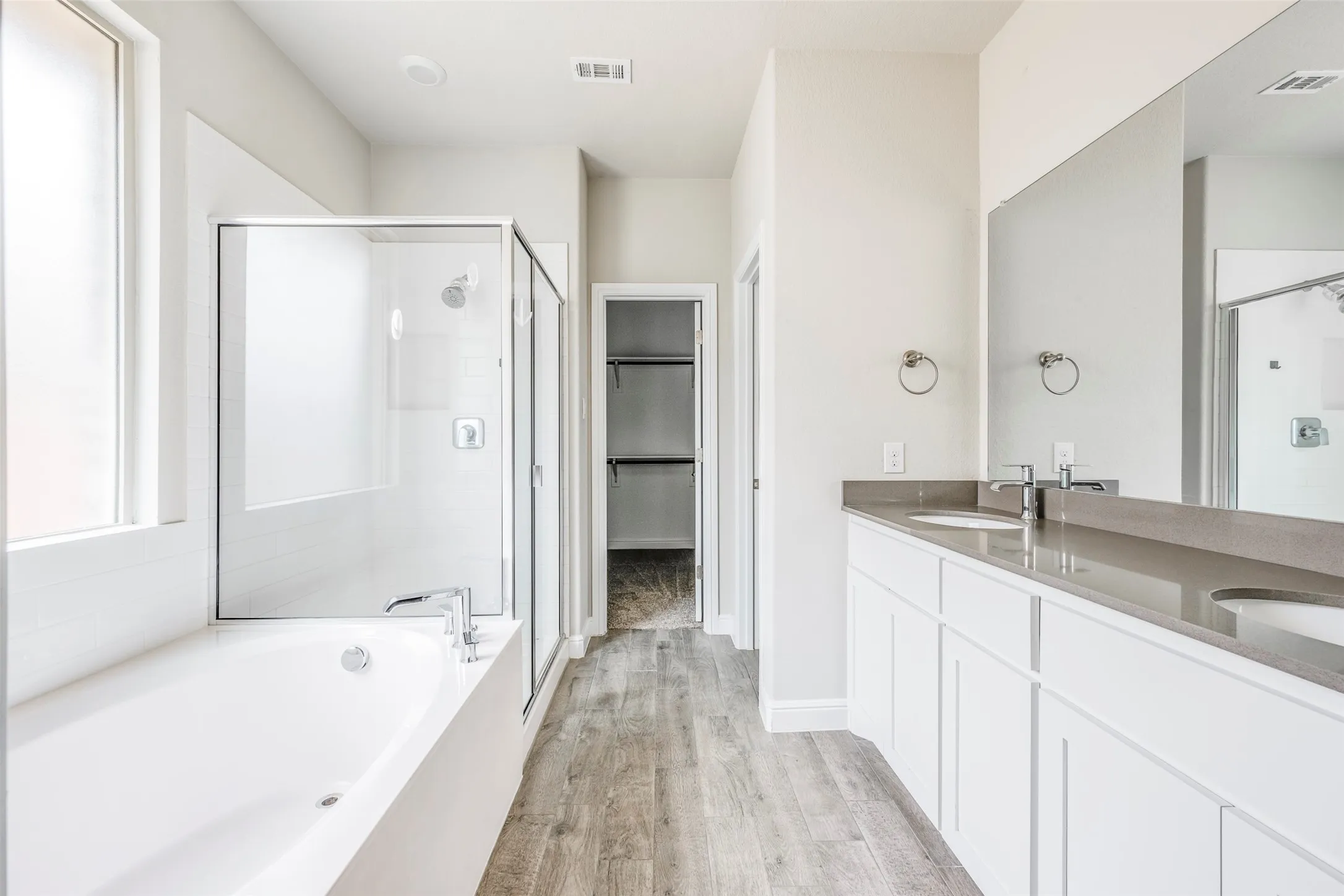 Spacious bathroom featuring a built-in soaking tub, a clear glass shower enclosure with tile surround, a dual vanity with undermount sinks, and wood-finish flooring