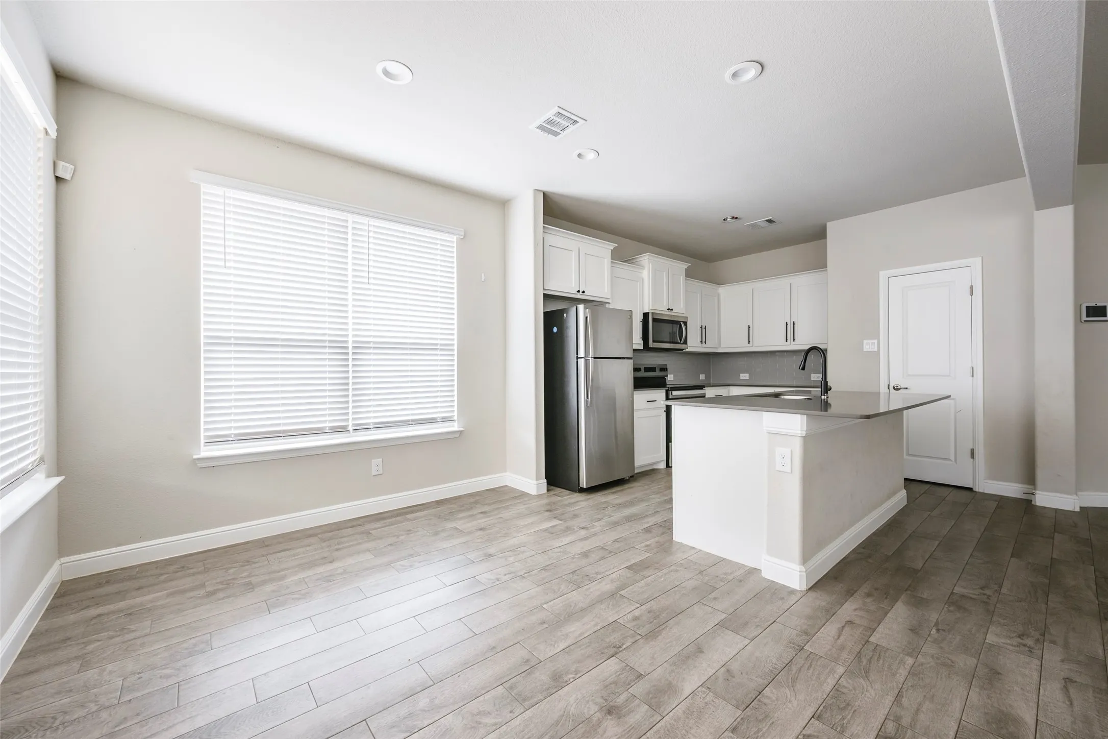 Open-concept living space featuring wood-finish flooring, recessed lighting, and a kitchen with white cabinetry, stainless steel appliances, and a central island with a dark countertop